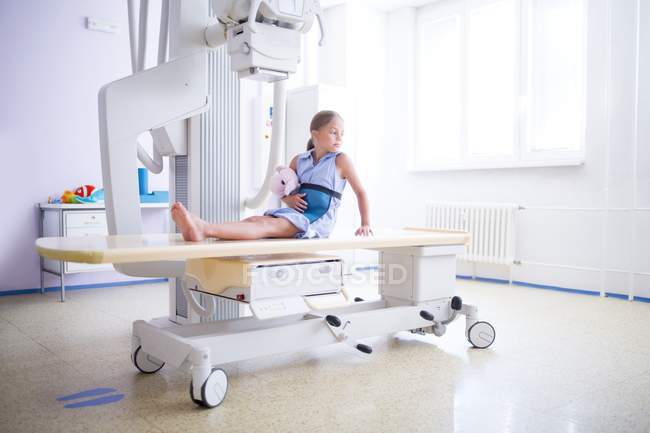 Girl holding teddy and waiting for x-ray therapy on bed. — Stock Photo