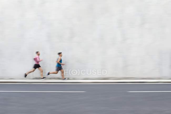 Atletas masculinos corriendo en la calle frente a la pared de hormigón - foto de stock