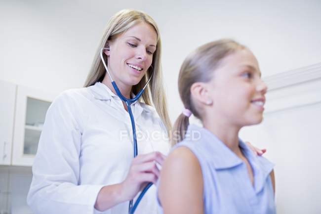 Female doctor examining young girl back with stethoscope. — Stock Photo
