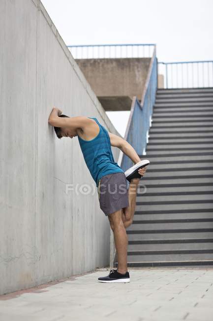 Hombre apoyado en la pared y estiramiento de la pierna . - foto de stock