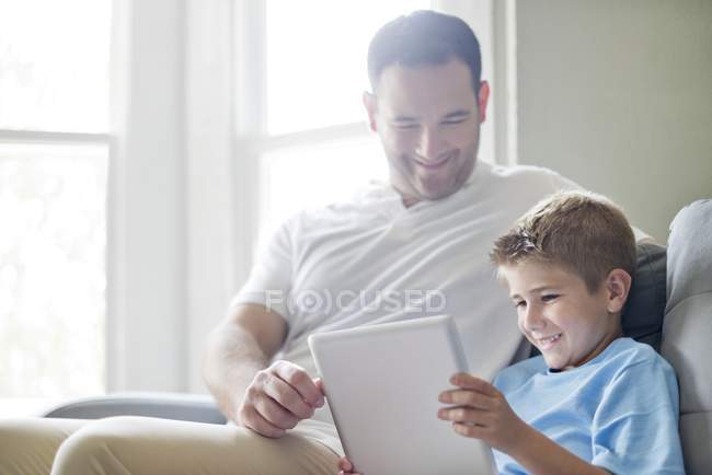 Батько і син використовують цифровий планшет на дивані . — стокове фото