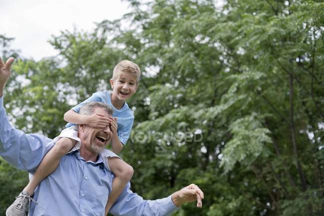 Boy covering grandfather eyes while sitting on shoulders. — Stock Photo