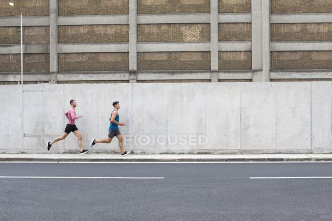 Atletas do sexo masculino correndo na rua em frente à construção — Fotografia de Stock
