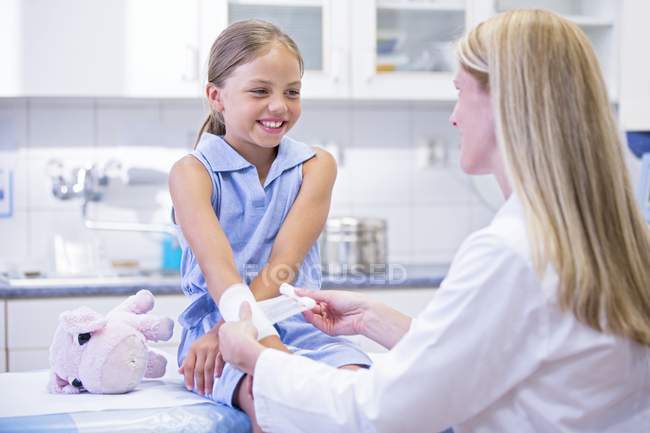Медсестра накладывает повязку на руку девочки младшего возраста . — стоковое фото