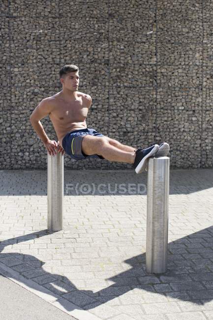 El hombre que equilibra en dos bolardos mientras que hace push-up inversa . - foto de stock