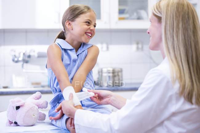 Enfermeira aplicando bandagem para braço menina idade elementar . — Fotografia de Stock