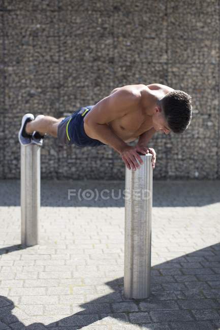Man balancing on two bollards while doing push-up. — Stock Photo