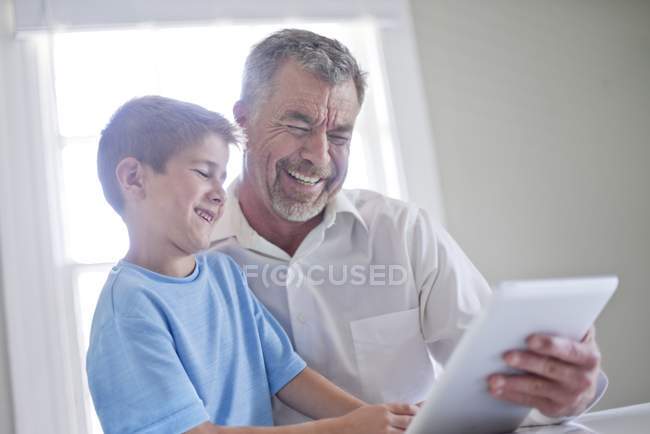 Grand-père et petit-fils utilisant une tablette numérique et souriant à l'intérieur . — Photo de stock
