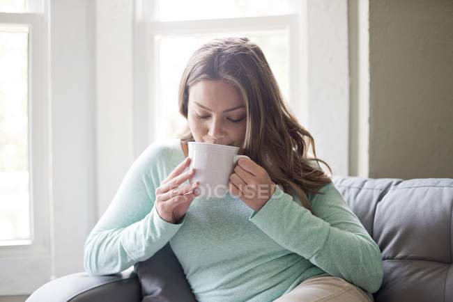 Mujer joven bebiendo bebida caliente de la taza . - foto de stock