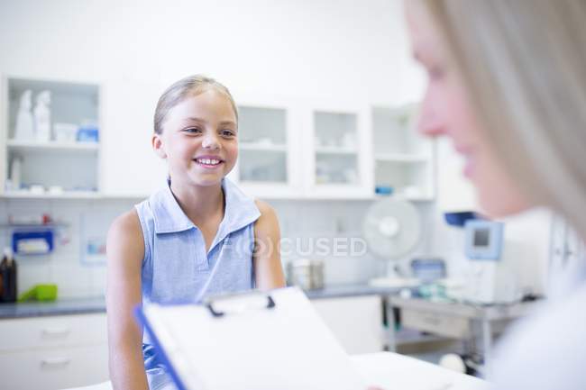 Female doctor with clipboard talking with young girl. — Stock Photo