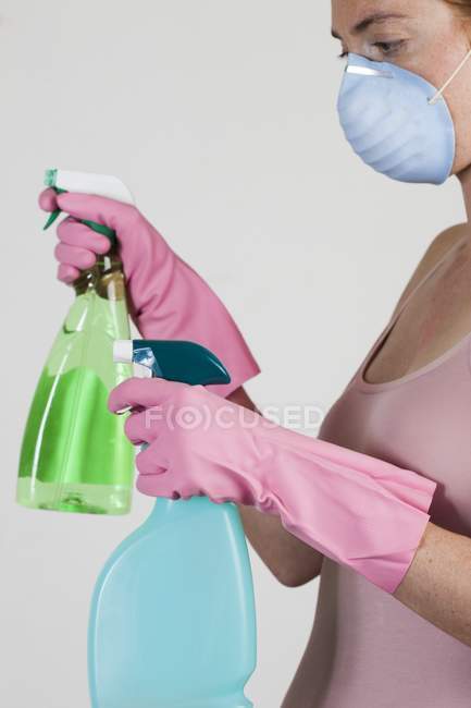 Close-up of woman wearing face mask holding cleaning materials in hands. — Stock Photo