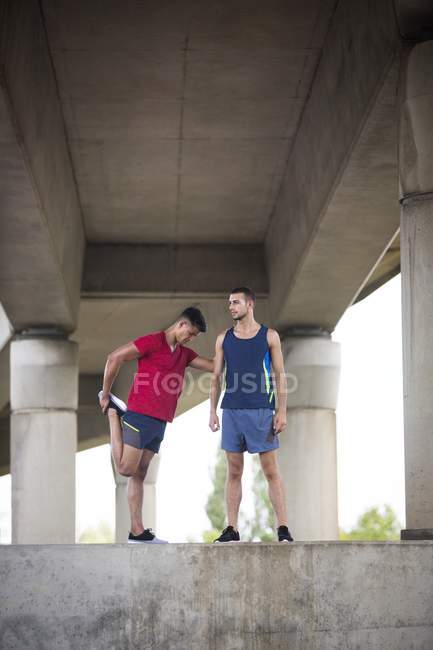 Atleti maschi che si allungano sotto il ponte di cemento . — Foto stock