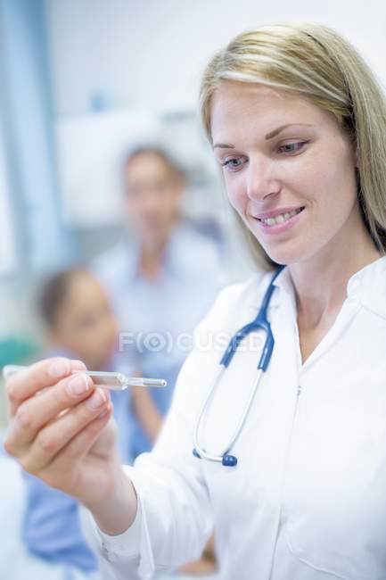 Doctor looking at thermometer with people in background. — Stock Photo