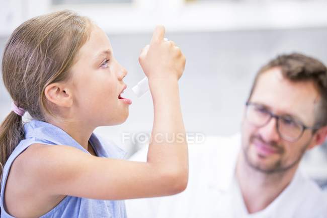 Chica usando inhalador mientras médico masculino viendo . - foto de stock