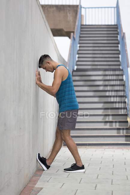 Man leaning on wall and stretching foot. — Stock Photo