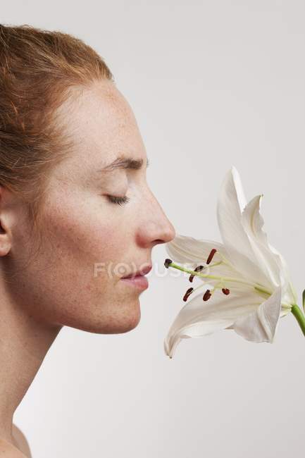 Mulher com os olhos fechados cheirando a flor branca, vista lateral . — Fotografia de Stock