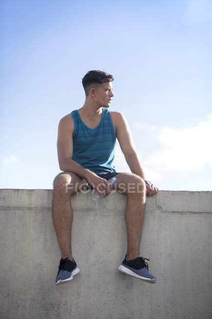 Uomo seduto sul tetto con una bottiglia d'acqua e guardando altrove . — Foto stock