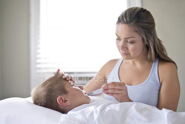 Мать, принимающая температуру сына в постели . — стоковое фото