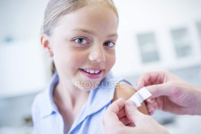 Person applying plaster to young girl shoulder. — Stock Photo