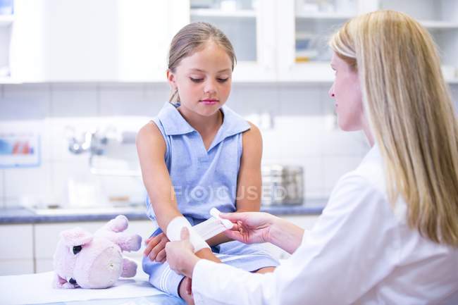 Infirmière appliquant un bandage au bras de la fille d'âge élémentaire . — Photo de stock