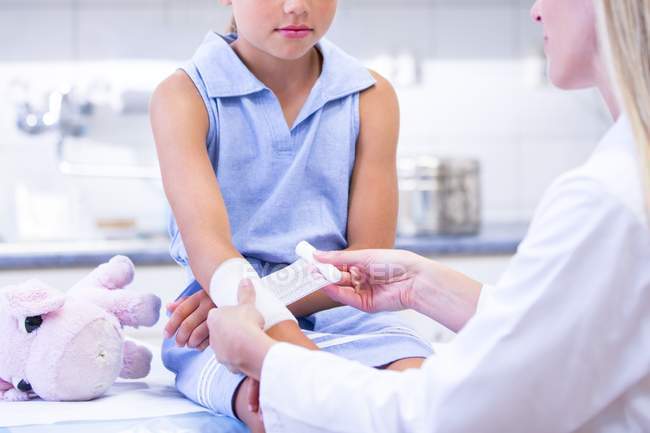 Nurse applying bandage to elementary age girl arm. — Stock Photo