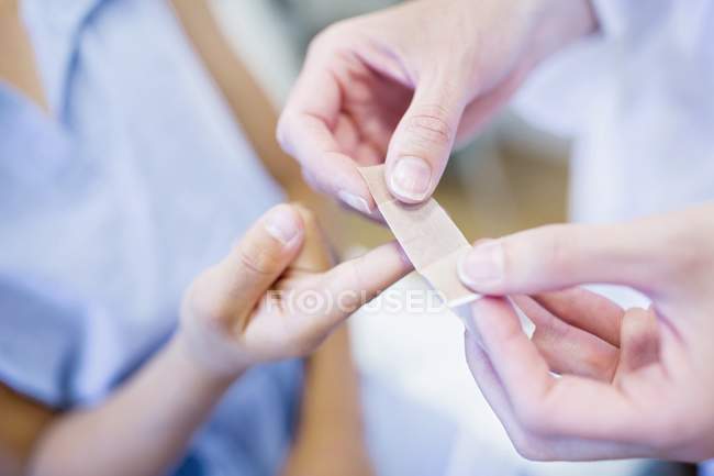 Person applying plaster to child hand. — Stock Photo