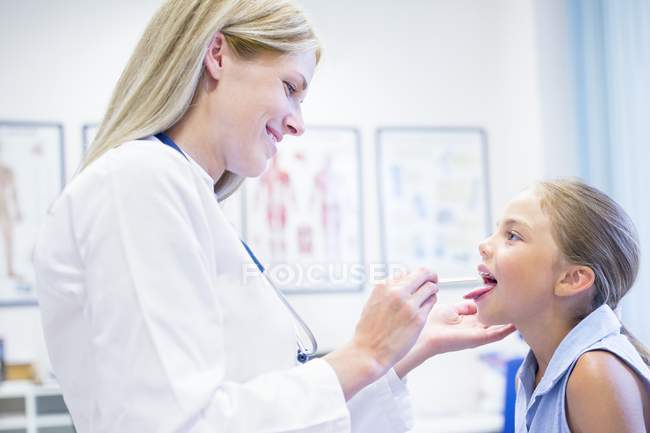 Mujer médico examinando joven chica lengua . - foto de stock