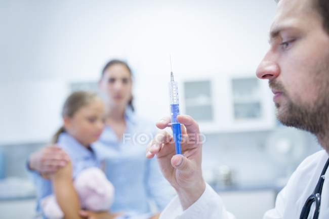 Médico do sexo masculino que prepara a injeção da seringa com pessoas no fundo . — Fotografia de Stock