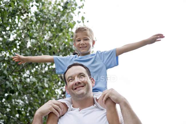 Father carrying son on shoulders with arms out. — Stock Photo