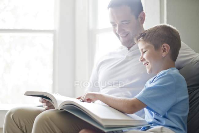 Filho ler livro com o pai no sofá . — Fotografia de Stock