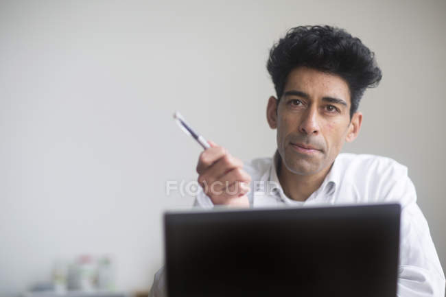 Portrait of male mid adult doctor sitting in office. — Stock Photo