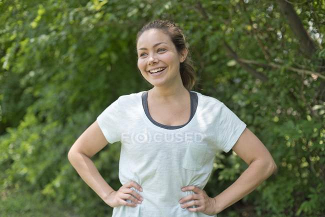 Молодая женщина с руками на бедрах улыбается на открытом воздухе . — стоковое фото