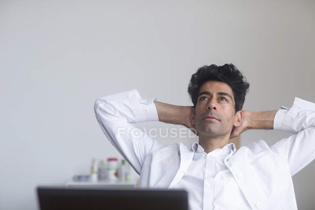 Doctor thinking at desk in office with hands behind head. — Stock Photo