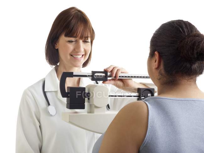 Female doctor weighing woman on scales. — Stock Photo