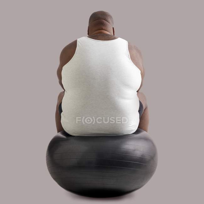 Homem com excesso de peso sentado na bola de exercício, visão traseira . — Fotografia de Stock