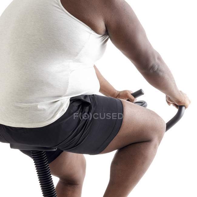 Overweight man on exercise bike, cropped. — Stock Photo