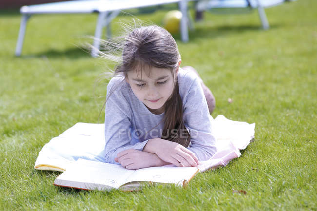 Chica preadolescente acostada en una manta en el prado verde en el jardín y libro de lectura . - foto de stock