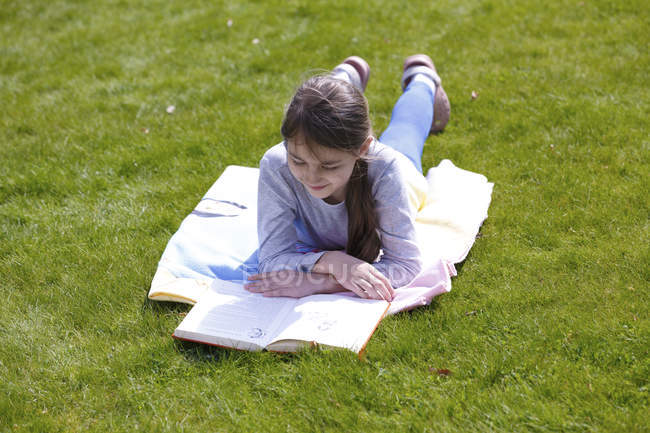 Frühchen liegt auf Decke auf grüner Wiese im Garten und liest Buch. — Stockfoto