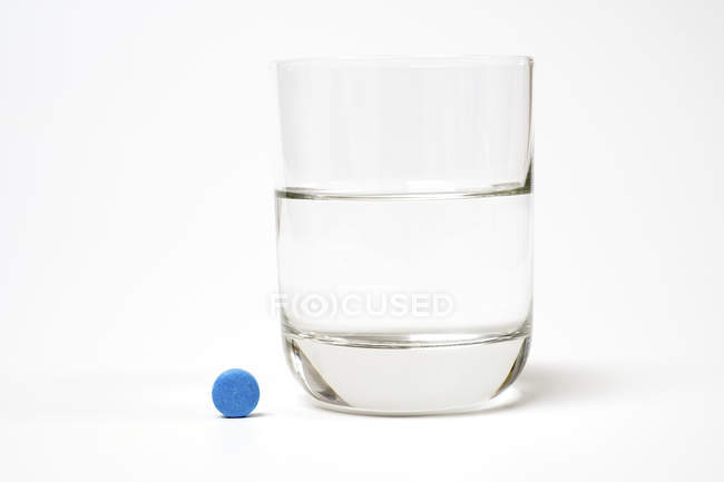 Pastilla azul y vaso de agua sobre fondo blanco
. - foto de stock