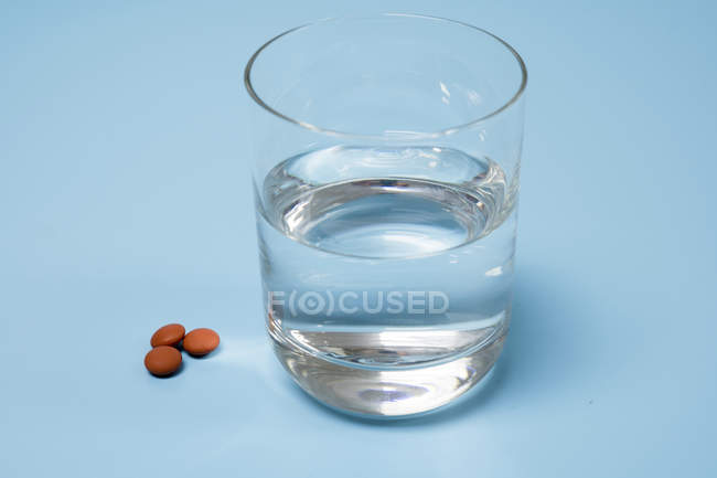 Pills and glass of water on blue background. — Stock Photo