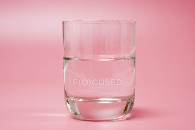 Bicchiere di acqua pulita su sfondo rosa . — Foto stock