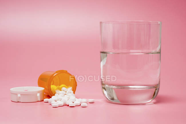 Medicamentos y vaso de agua sobre fondo rosa . - foto de stock