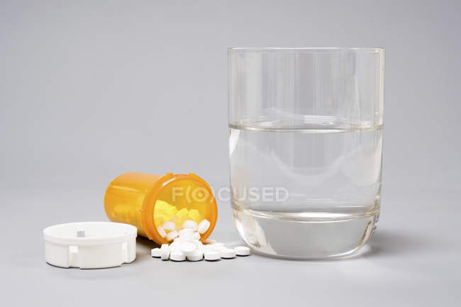 Medicamentos y vaso de agua sobre fondo blanco . - foto de stock