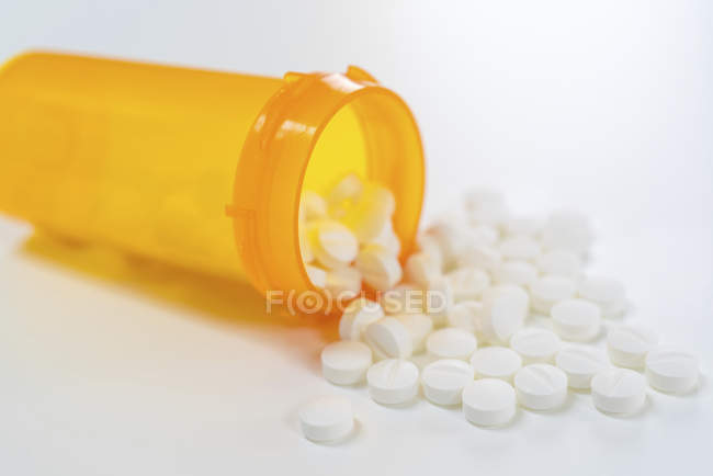 Pílulas brancas derramando de recipiente de plástico aberto . — Fotografia de Stock