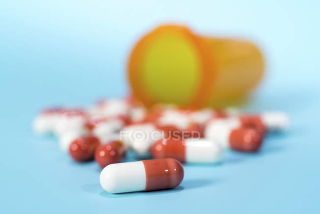 Drug capsules spilling from plastic cup on blue background. — Stock Photo
