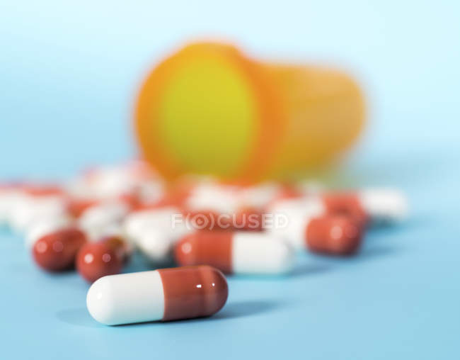 Medikamentenkapseln verschüttet aus Plastikbecher auf blauem Hintergrund. — Stockfoto