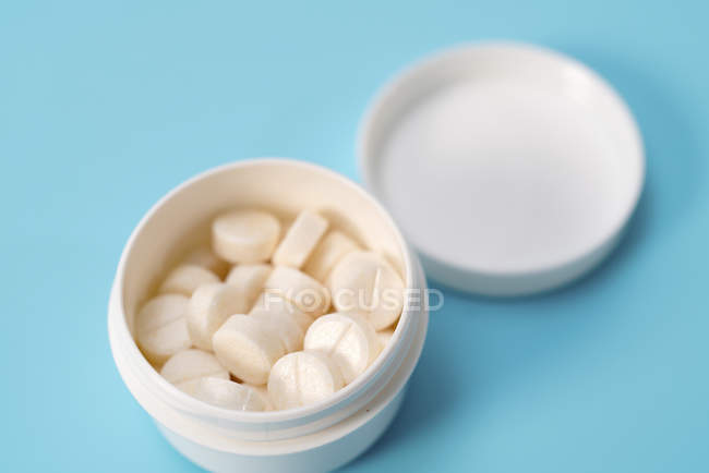 Weiße Tabletten in einem Plastikbehälter auf blauem Hintergrund. — Stockfoto