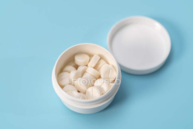 Comprimidos brancos num recipiente de plástico sobre fundo azul
. — Fotografia de Stock
