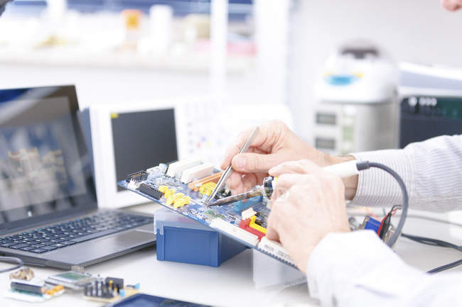 Primer plano del técnico que repara la placa de circuito en el laboratorio de electrónica . - foto de stock