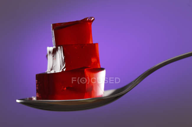 Cubos de gelatina roja en cuchara sobre fondo púrpura . - foto de stock